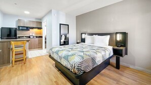 A modern hotel room with a bed, bedside table, and a kitchenette area. - Motel 6 Duluth, GA- Atlanta- Gwinnett Place (Duluth)