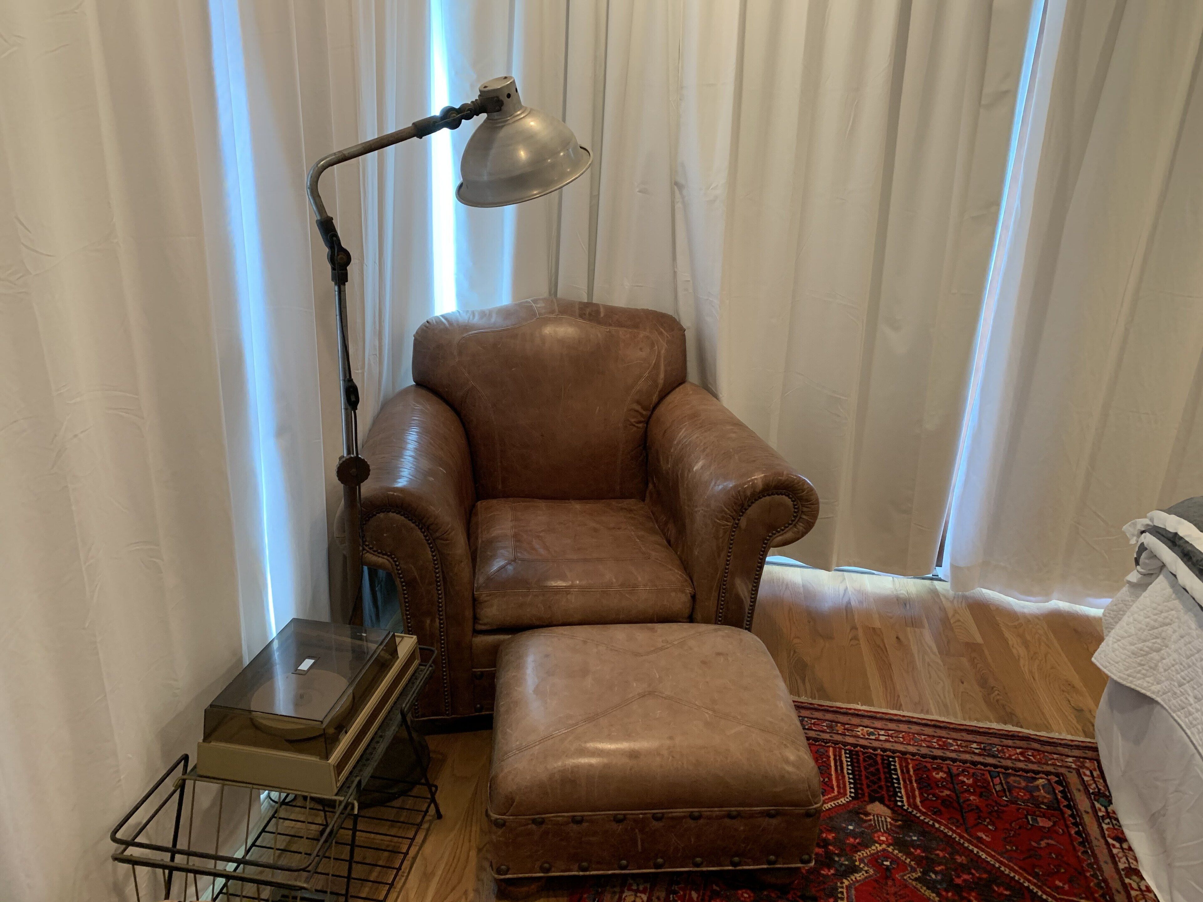 Ein Ledersessel mit Hocker in einem Raum mit Stehlampe, einem kleinen Tisch und einem gemusterten Teppich.