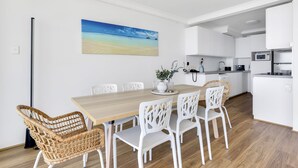 A modern kitchen with white cabinetry, a wooden dining table, and wicker chairs.