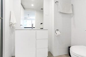 Une salle de bain moderne avec des carreaux blancs, un lavabo avec un miroir, des toilettes et un espace douche.