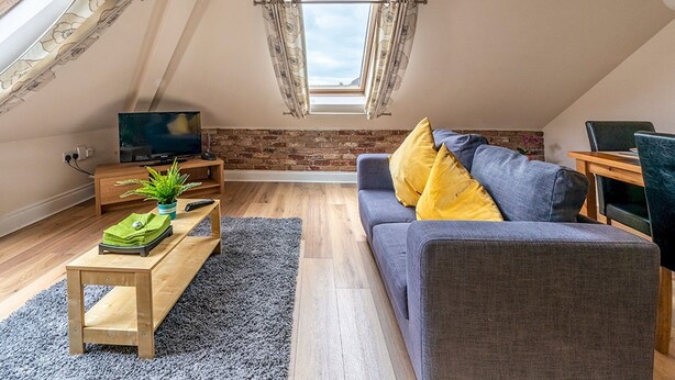 Un dormitori d'estil loft modern amb sostre inclinat, una finestra gran, un llit i un escriptori amb una planta.