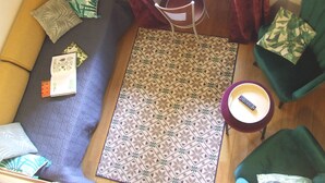 Une pièce avec un tapis à motifs, un canapé, un fauteuil, une petite table avec une télécommande et un ordinateur portable posé sur un bureau.