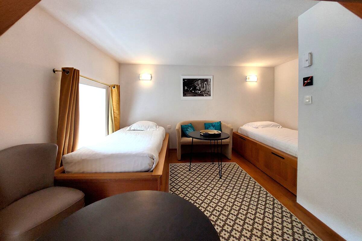 Una habitación de hotel compacta con dos camas individuales, un sofá, una mesita pequeña y una alfombra estampada.