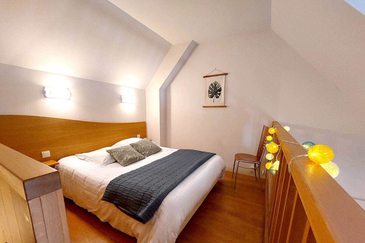 Un dormitorio con cama, mesitas de noche, una silla, una lámpara de pared y un objeto decorativo.