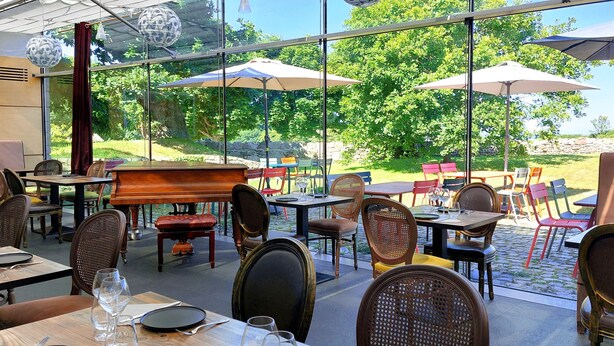 Un espace de restauration en plein air avec des tables et des chaises, de grands parasols et une vue sur la verdure.