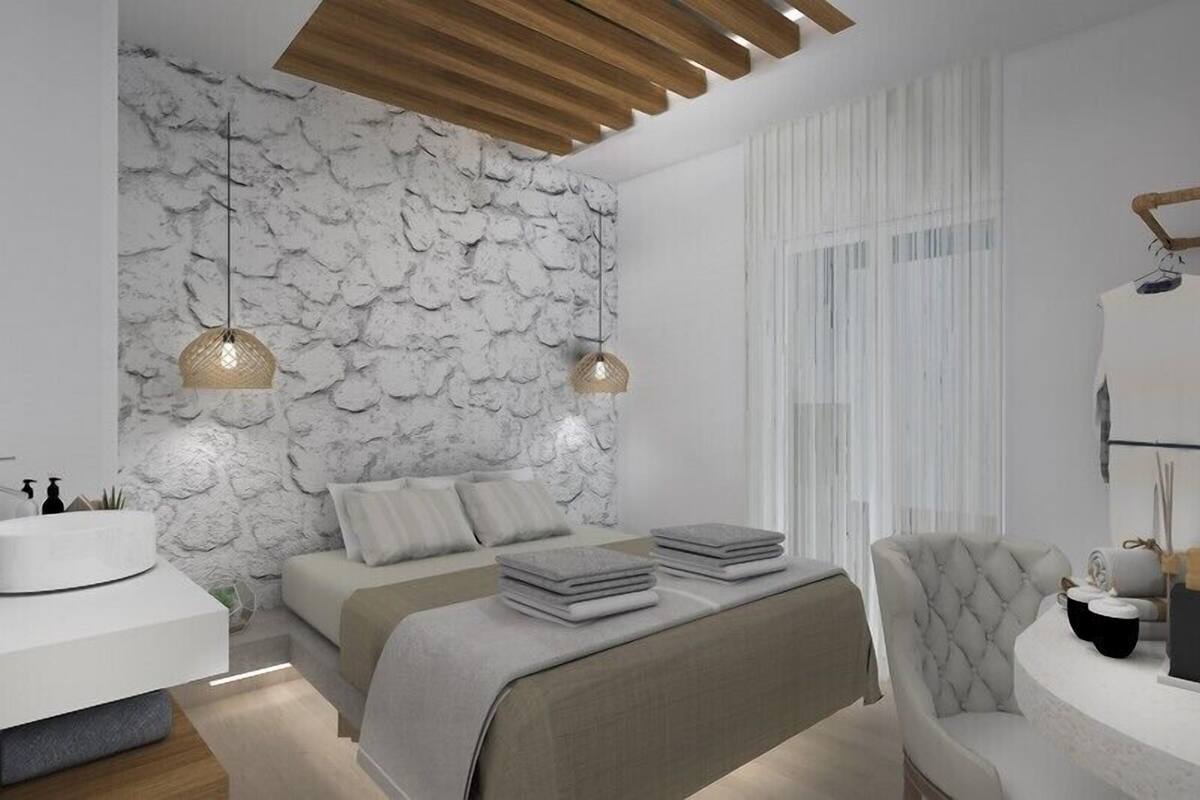 A modern bedroom with a stone wall, a bed with grey bedding, a white bedside table, and two hanging lamps.
