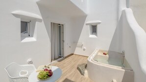 Una habitación moderna con paredes blancas, una bañera, una pequeña mesa con un frutero y una puerta que conduce a otra habitación.