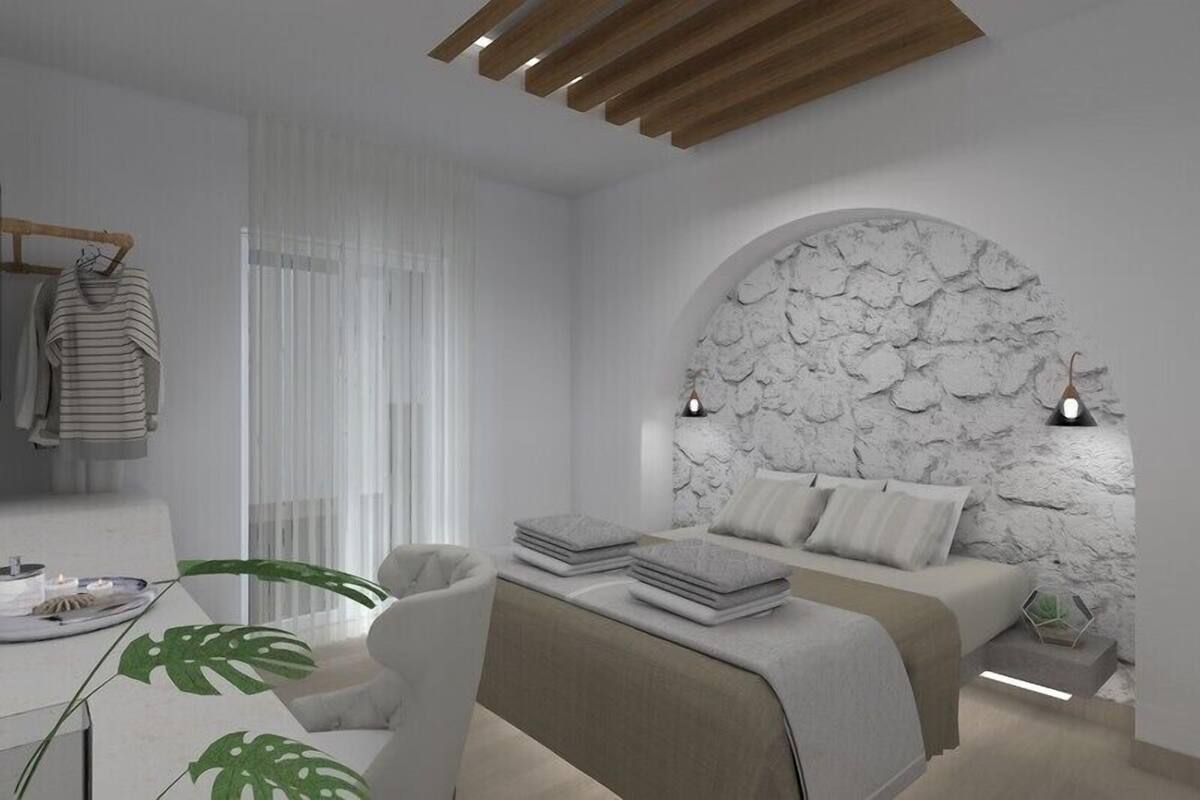 A modern bedroom with a stone wall, a bed with pillows, a bedside table, and a hanging rack with clothes.