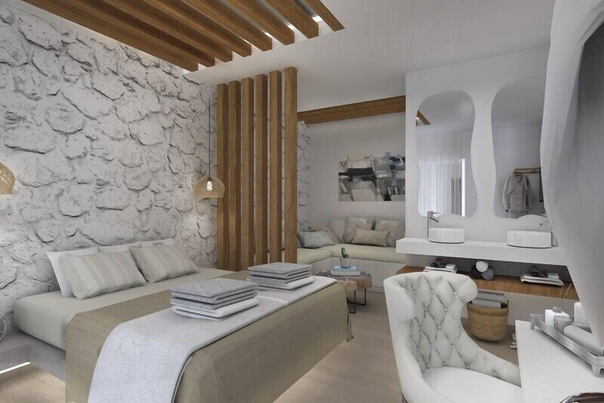 A modern bedroom with a stone wall, a bed with a headboard, a seating area with a sofa, and a vanity with a mirror.