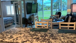 A kitchen with granite countertops, a dining area with a table and chairs, a television mounted on the wall, and a view of the outdoors through large windows.