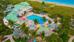 A resort with a swimming pool, lounge chairs, and palm trees.