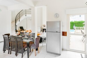 Uma cozinha moderna com frigorífico embutido, área de refeições com cadeiras de madeira e escada que dá para um andar superior.