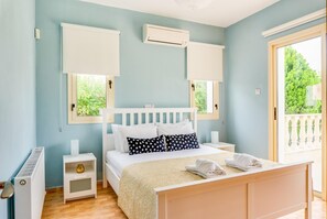 A bedroom with a bed, bedside tables, an air conditioning unit, and a view of greenery through the window.