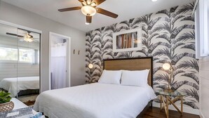 Un dormitorio con cama, ventilador de techo, espejo y papel tapiz tropical.