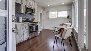 Una cocina moderna con muebles blancos, un microondas y una estufa. Hay un comedor con una mesa y sillas.