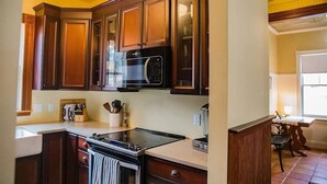A kitchen with wooden cabinets, a microwave, a stove, and a coffee maker. - Your Beautiful Victorian Getaway (Bethel)