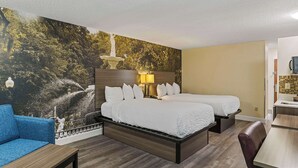 A hotel room with a large bed, a blue armchair, a wooden desk, and a mural of a fountain and trees. - Clarion Pointe Savannah Gateway I-95 (Savannah)