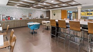 A modern restaurant with a central island, wooden flooring, and a mix of metal and wooden chairs. - Clarion Pointe Savannah Gateway I-95 (Savannah)