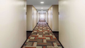 A long, narrow hallway with patterned carpet and beige walls. - Clarion Pointe Savannah Gateway I-95 (Savannah)