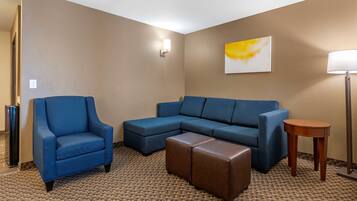 A hotel room with a blue armchair, a sectional sofa, and a small wooden side table.