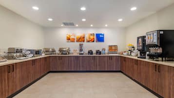 A modern breakfast area with a long counter, coffee machines, and a juice dispenser.