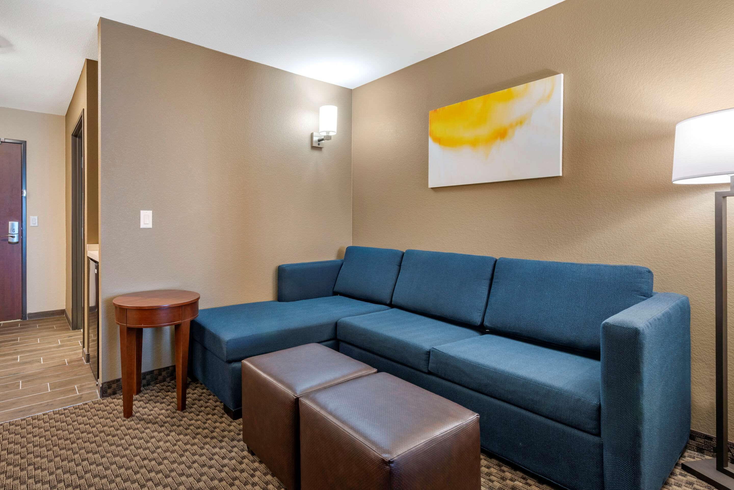 A modern hotel room with a blue sectional sofa, a wooden side table, and a brown leather ottoman.
