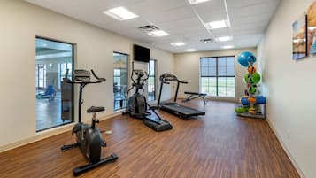 A gym with exercise equipment, large windows, and a wooden floor.