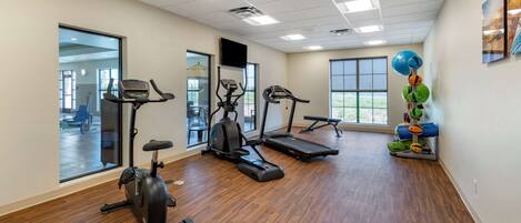A gym with exercise equipment, large windows, and a wooden floor.