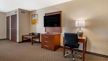 A hotel room with a desk, chair, dresser, TV, and lamp.