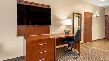 A hotel room with a wooden desk, a flat-screen TV, a lamp, a chair, and a carpeted floor.