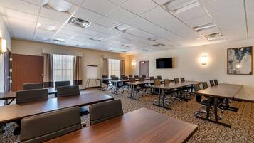 A conference room with multiple tables and chairs, a large screen, and a painting on the wall.