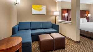 A hotel room with a blue sofa, a wooden side table, a brown ottoman, a bed, and a wall-mounted lamp. - Comfort Suites Broomfield-Boulder/Interlocken (Broomfield)