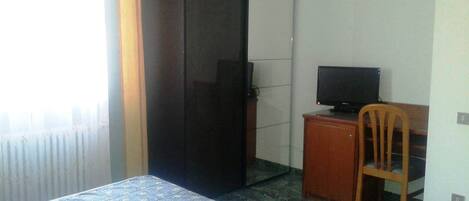 A hotel room with a bed, a desk with a television, a wardrobe, and a window with curtains.