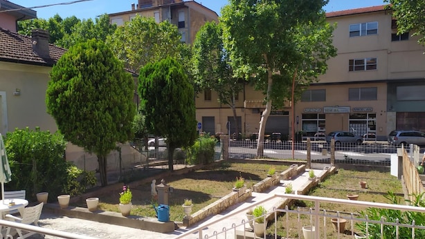 A courtyard with potted plants, a small table, and chairs. There are buildings in the background, including a car dealership and a bank. - Bed & Breakfast Domus Cesena (Cesena)