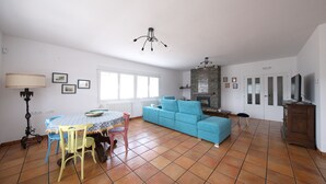 A spacious living room with a blue sofa, a dining table with chairs, a fireplace, and a television. - Villalbeja Casa Rural (Villalba de la Sierra)