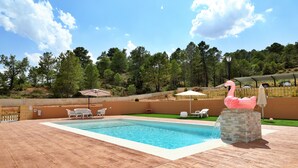 A swimming pool with a stone wall, lounge chairs, and a pink flamingo statue. - Villalbeja Casa Rural (Villalba de la Sierra)
