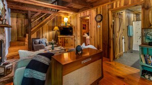 L’intérieur d’un chalet accueillant, avec un escalier en bois, un espace de vie comprenant un canapé et un téléviseur, et une salle de bain avec une douche et une horloge.