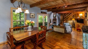 Une table à manger en bois, entourée de chaises, un lustre et un vase rempli de fleurs. On aperçoit une porte sur laquelle est inscrit « SALLE DE DÉGUSTATION » et un canapé au fond de la pièce.