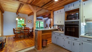 Une cuisine avec des poutres en bois, un coin repas avec une table et des chaises, et une poubelle.