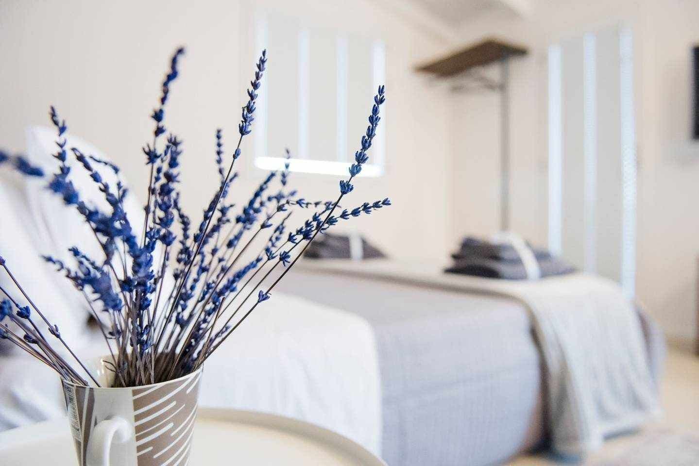 A room with a bed, a bedside table, and a vase with lavender flowers.