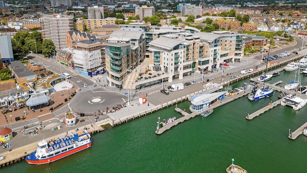 A waterfront cityscape with modern buildings, a marina, and a large red and white boat docked at the pier. - Steep Holm - With Spacious Balcony (Poole)