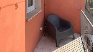 Un balcón con una sola silla, un ventanal y una lámpara colgante.