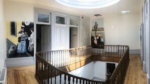 A spacious interior with a wooden staircase, white doors, and a mural on the wall. - NorteSoul Mouzinho (Porto)