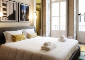 A neatly made bed with white linens and two pillows, a framed picture above the bed, and a window with curtains. - NorteSoul Mouzinho (Porto)