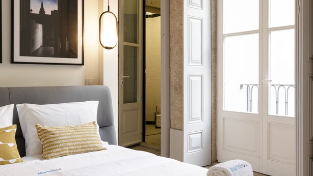 A hotel room with a neatly made bed, a framed picture on the wall, and a large window with a view. - NorteSoul Mouzinho (Porto)