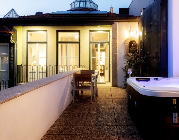 Un balcon avec un jacuzzi, une table et des chaises, et un bâtiment dont les fenêtres sont illuminées et qui est surmonté d’une coupole, le tout sur fond de paysage.