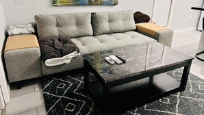 Una sala de estar moderna con un sofá gris, una mesa de centro negra y un cuadro con una playa.
