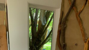 Una habitación con una cama grande, un banco de madera, una mesita y vista a un árbol.