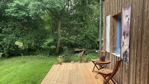Una terraza de madera con una mesa y sillas, rodeada de follaje y una valla de madera.