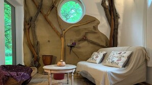 Una habitación acogedora con un ventanal redondo, un sofá con cojines estampados, una mesita con una lámpara y una silla de mimbre.